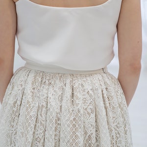 May include: A white sleeveless top with a white lace skirt. The skirt has a delicate floral pattern.