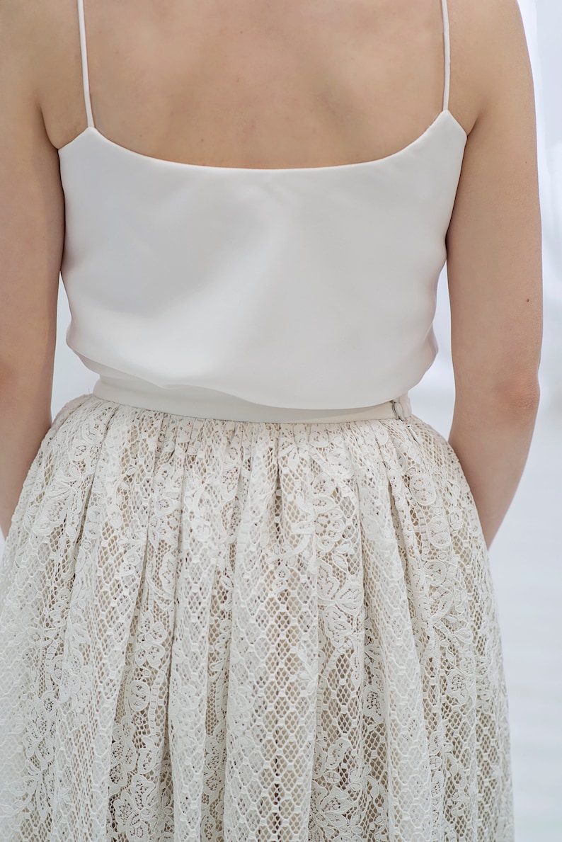 May include: A white sleeveless top with a white lace skirt. The skirt has a delicate floral pattern.