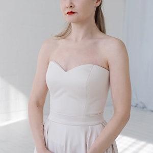 Puede incluir: Una mujer con un vestido de novia de sat&eacute;n marfil sin tirantes con escote de coraz&oacute;n. El vestido tiene un corpi&ntilde;o ajustado y una falda completa.