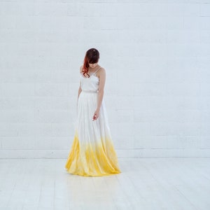May include: A woman wearing a white dress with a yellow ombre effect. The dress is a simple, sleeveless design with a fitted bodice and a flowing skirt.