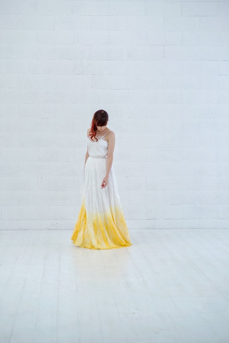 May include: A woman wearing a white dress with a yellow ombre effect. The dress is a simple, sleeveless design with a fitted bodice and a flowing skirt.