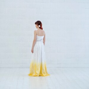 May include: A white maxi skirt with a yellow ombre effect. The skirt is made of a lightweight fabric and has a flowy silhouette.