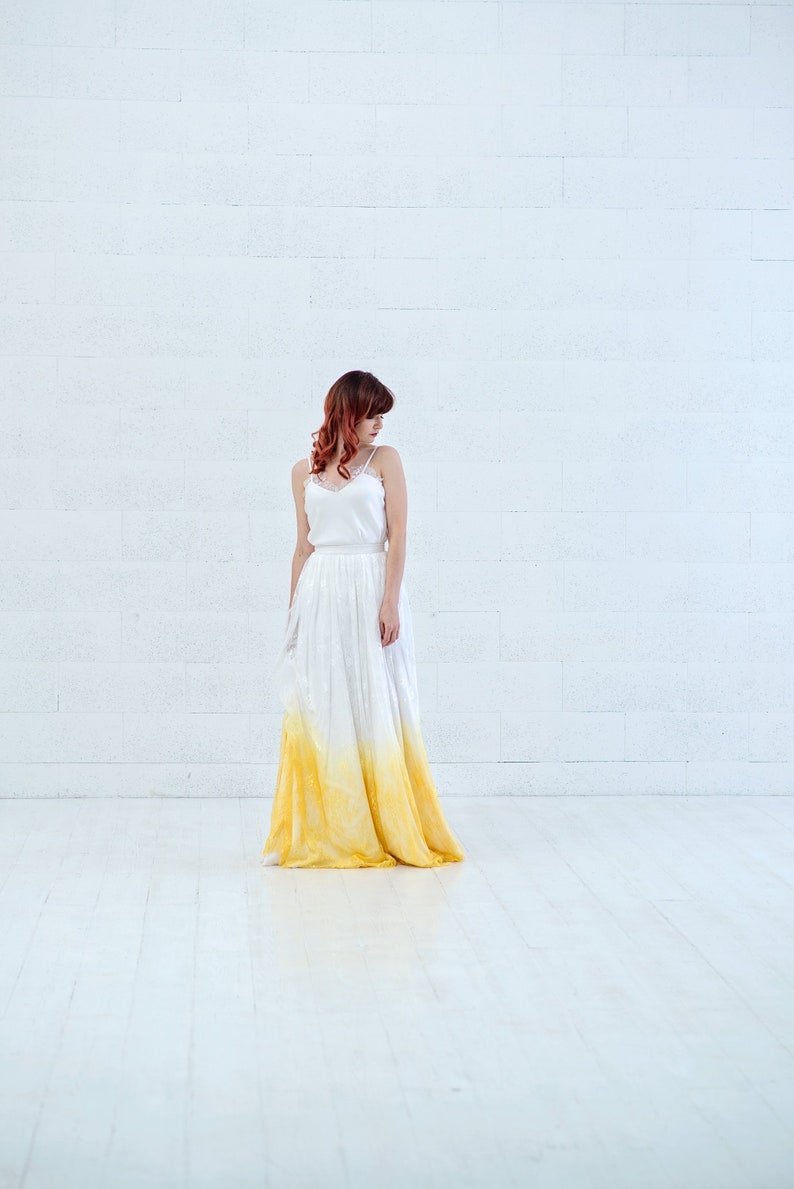 May include: A woman wearing a white and yellow ombre wedding dress with a lace bodice. The dress is flowing and has a relaxed fit.