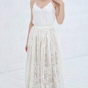 May include: A white lace skirt with a satin waistband. The skirt is long and flowing, and the lace is delicate and intricate.