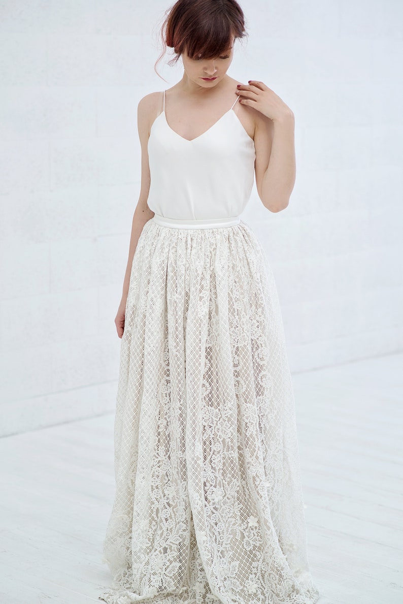 May include: A white lace skirt with a satin waistband. The skirt is long and flowing, and the lace is delicate and intricate.