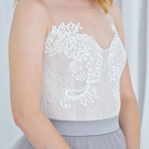 May include: A white lace bodice with a gray tulle skirt. The bodice has a sweetheart neckline and delicate floral lace detailing.