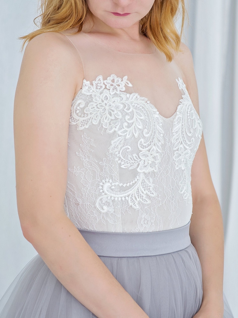 May include: A white lace bodice with a gray tulle skirt. The bodice has a sweetheart neckline and delicate floral lace detailing.