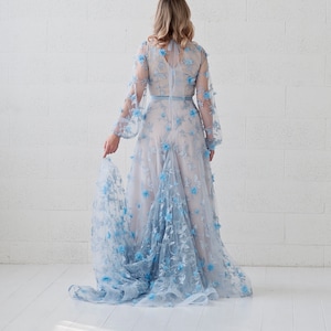 May include: A light blue maxi dress with floral embroidery. The dress has a fitted bodice and a flowing skirt. The dress is made of a sheer fabric and has a delicate lace trim.