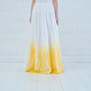 May include: A white lace skirt with a yellow ombre dye effect. The skirt is long and flowing, and the dye starts at the bottom and fades to white at the top.