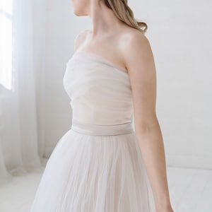 Puede incluir: Un vestido de novia blanco de tul sin tirantes con una banda de sat&eacute;n. El vestido tiene una falda fluida y es perfecto para una novia que quiere un look rom&aacute;ntico y elegante.