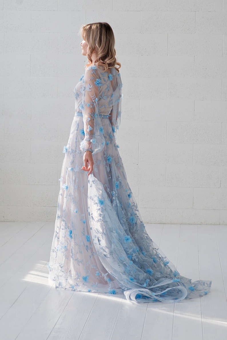 May include: A woman wearing a light blue gown with floral embroidery. The gown has a long train and is made of a sheer fabric.
