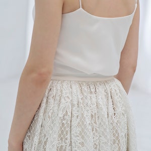 May include: A white sleeveless top with a lace skirt. The skirt has a delicate floral pattern.