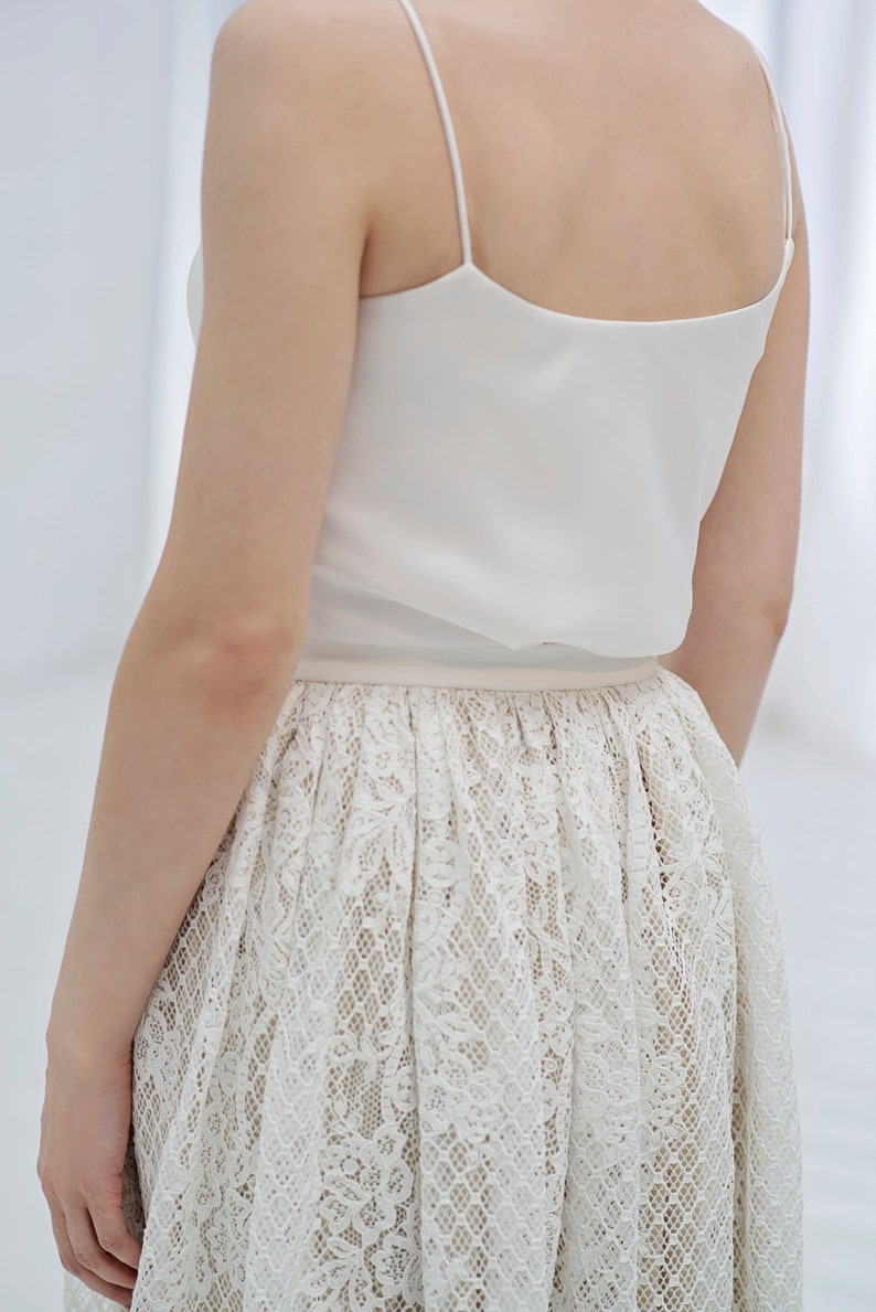 May include: A white sleeveless top with a lace skirt. The skirt has a delicate floral pattern.