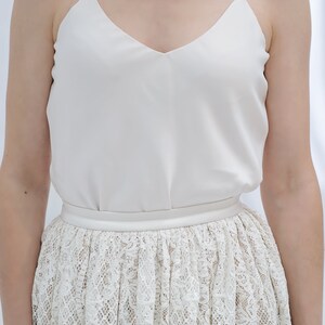 May include: A white sleeveless top with a V-neckline and a white lace skirt.