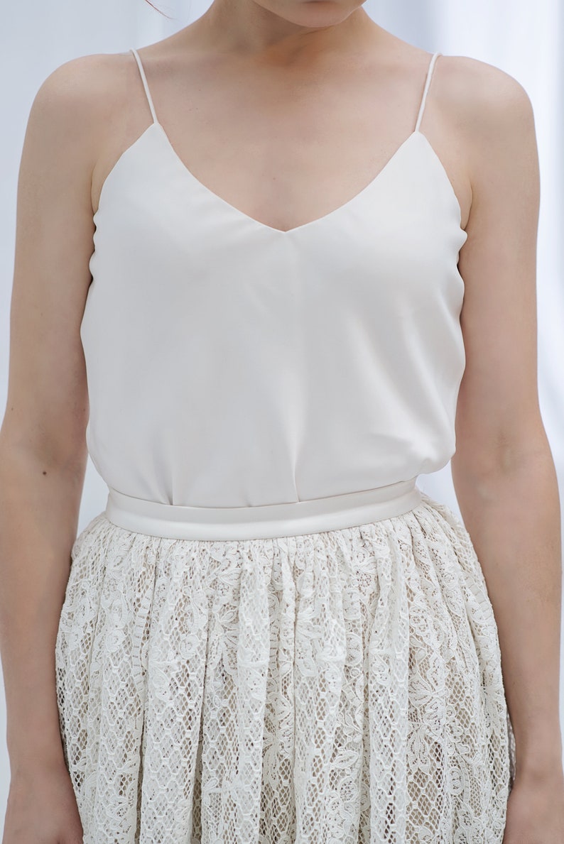 May include: A white sleeveless top with a V-neckline and a white lace skirt.