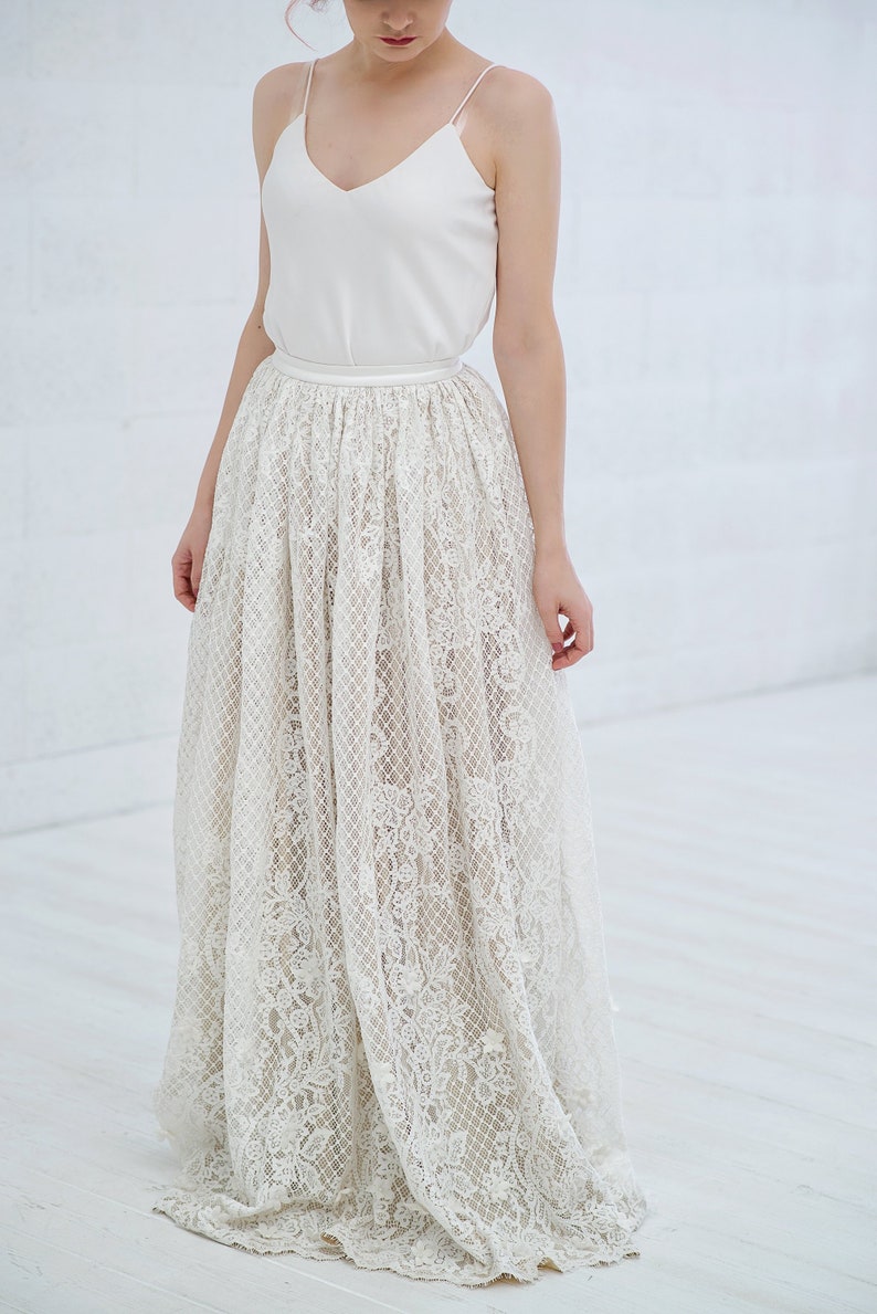 May include: A white lace skirt with a satin waistband. The skirt is floor-length and has a delicate floral pattern.
