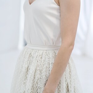 May include: A white sleeveless top with a V-neckline and a lace skirt. The skirt is a full skirt with a delicate floral pattern.