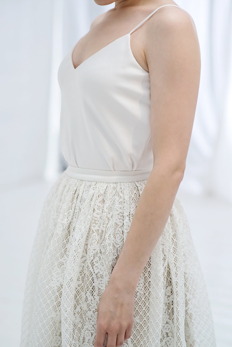 May include: A white sleeveless top with a V-neckline and a lace skirt. The skirt is a full skirt with a delicate floral pattern.