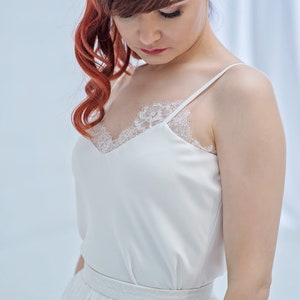 May include: A white satin top with a lace trim neckline and thin straps. The top is paired with a white tulle skirt with lace detailing.