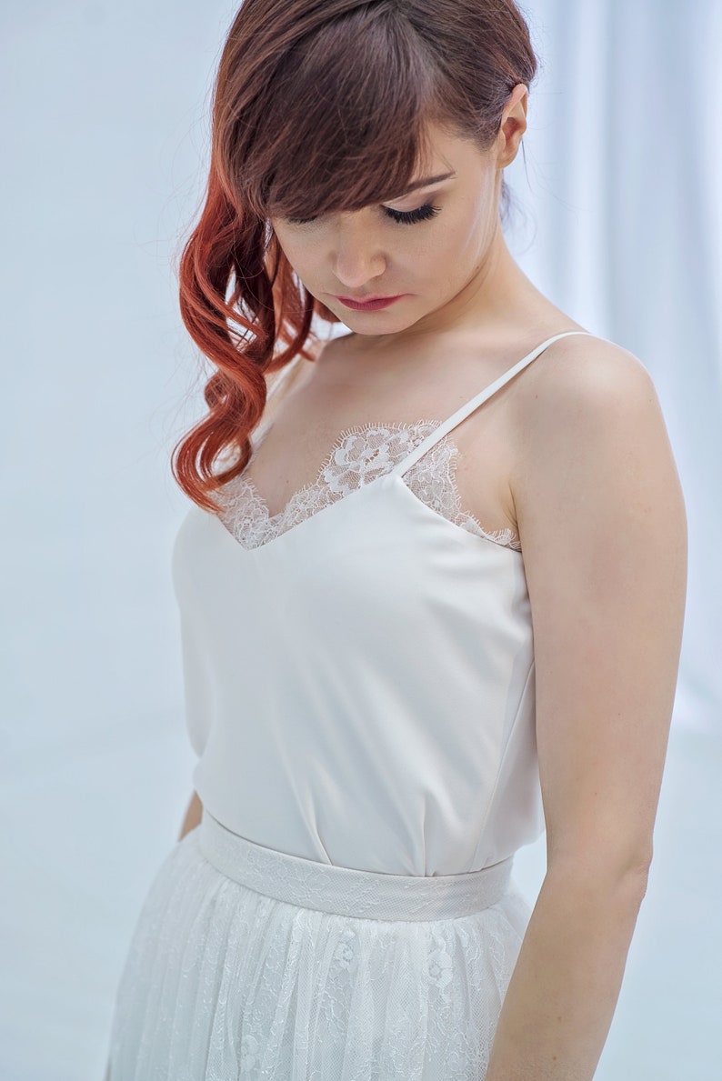 May include: A white satin top with a lace trim neckline and thin straps. The top is paired with a white tulle skirt with lace detailing.