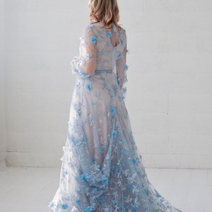 May include: A light blue gown with a floral design. The gown has a long skirt and long sleeves. The gown is made of a sheer fabric and has a fitted bodice.
