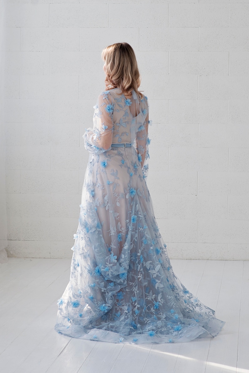 May include: A light blue gown with a floral design. The gown has a long skirt and long sleeves. The gown is made of a sheer fabric and has a fitted bodice.