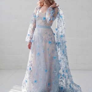 May include: A light blue maxi dress with floral embroidery. The dress has long sleeves and a fitted bodice. The skirt is full and flowing.