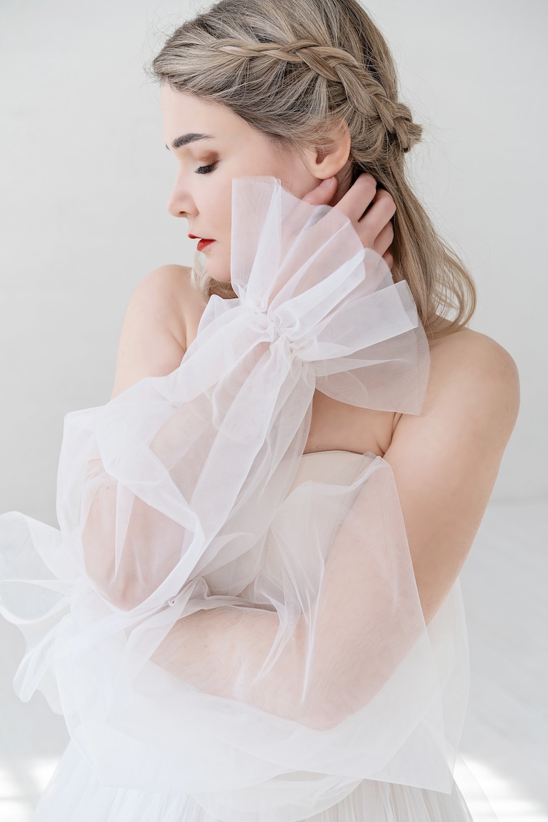 Puede incluir: Una manga de novia de tul blanco con un dise&ntilde;o de volantes. La manga es transparente y delicada, y ser&iacute;a una hermosa adici&oacute;n a cualquier vestido de novia.