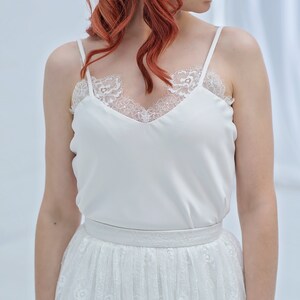 May include: A white lace top with a satin bodice and a white tulle skirt with floral embroidery.