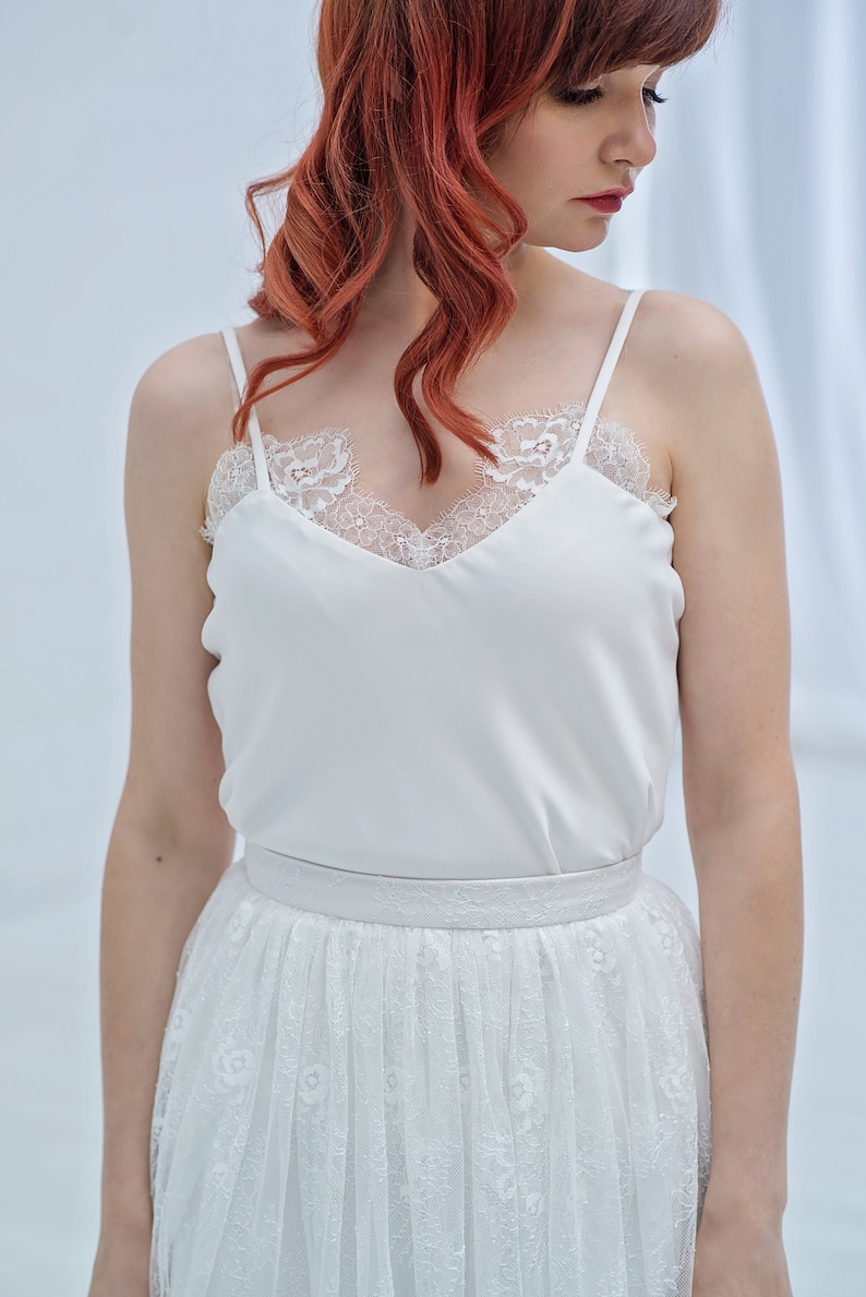 May include: A white lace top with a satin bodice and a white tulle skirt with floral embroidery.