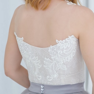May include: A white lace bodice with a gray tulle skirt and a satin waistband. The waistband has three buttons.