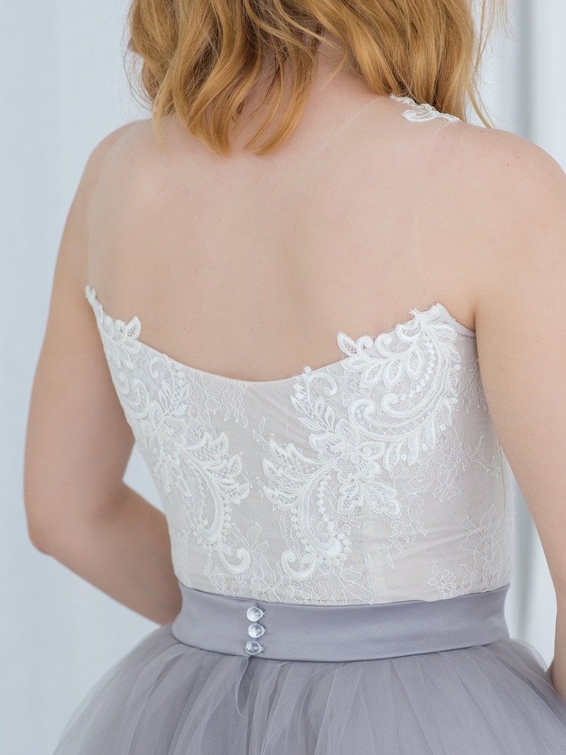 May include: A white lace bodice with a gray tulle skirt and a satin waistband. The waistband has three buttons.