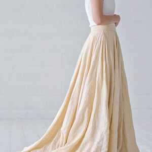 May include: A cream-colored, floor-length skirt with a subtle floral pattern. The skirt is paired with a white, textured camisole top. The skirt has a high waist and a flowing silhouette, suitable for formal occasions.