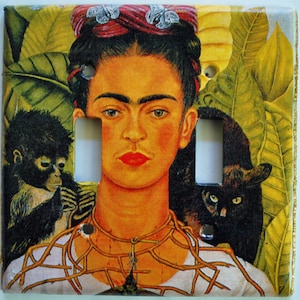 May include: A light switch cover featuring a colorful portrait of Frida Kahlo with a monkey and a black cat. The background is a vibrant green with leaves.