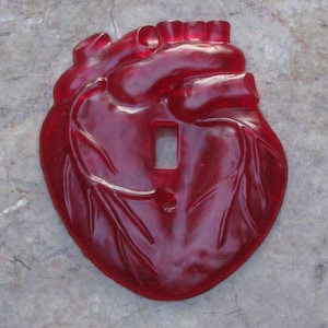 May include: A red plastic light switch cover shaped like a human heart.