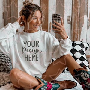 Puede incluir: Una sudadera blanca con el texto "YOUR DESIGN HERE" impreso en la parte delantera. La sudadera la lleva puesta una persona que lleva botas de vaquero.