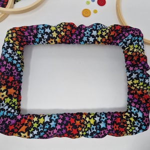 May include: A black embroidery hoop with a colorful star print fabric cover. The fabric is a rainbow of colors with multi-colored stars on a black background.
