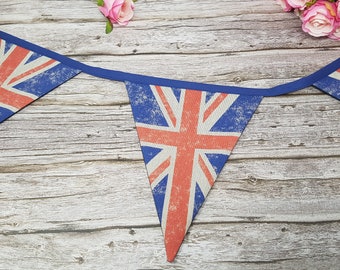 May include: A bunting with a vintage look featuring the Union Jack flag in red, white, and blue. The bunting is made of fabric and has a blue ribbon running through it. The bunting is hanging on a wooden surface.