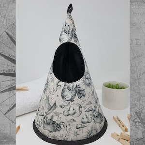 May include: A white cone-shaped pet bed with a black fabric lining and a black trim. The fabric features a black and white print of celestial bodies, including stars, moons, and a ship.