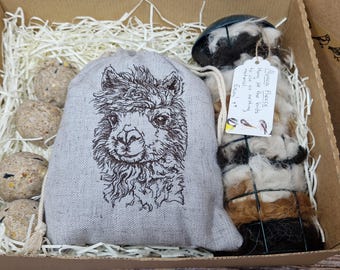 May include: A gift box containing a gray linen bag with an embroidered llama face, several birdseed balls, and a bundle of alpaca fleece. The fleece has a tag that reads "Alpaca Fleece, Hay for the birds to use as nesting material. Enjoy it!"