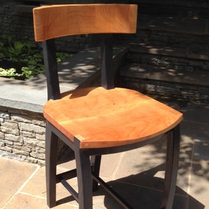 May include: A wooden chair with a black stained frame and a natural wood seat. The chair has a curved back and a simple design.