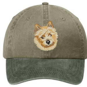 May include: A two-tone baseball cap in olive green and darker green. The cap features an embroidered image of a dog's face in shades of tan and brown. The cap has a curved brim and an adjustable strap.