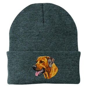 May include: A dark gray knit beanie featuring an embroidered image of a brown and tan dog's head. The dog has a pink tongue and is facing right. The beanie has a folded cuff.