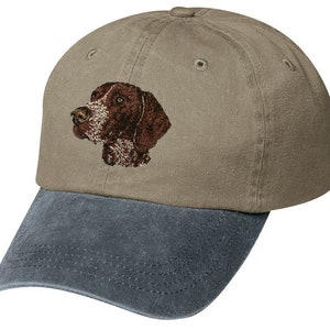 May include: A brown and white German Shorthaired Pointer dog embroidered on a khaki baseball cap with a dark blue denim bill.