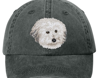 May include: A dark gray baseball cap featuring an embroidered image of a fluffy white dog's face. The dog has brown eyes and a black nose. The cap has a curved brim and an adjustable strap.