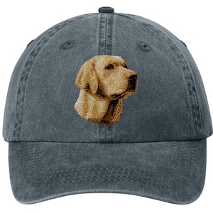 May include: A charcoal grey baseball cap featuring an embroidered golden yellow Labrador retriever head in profile. The cap has a six-panel construction with a curved brim and a button on the top center, showcasing a detailed stitched dog portrait.
