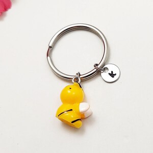 May include: A silver key chain with a small yellow and black bee charm and a silver charm with the letter "K" on it.