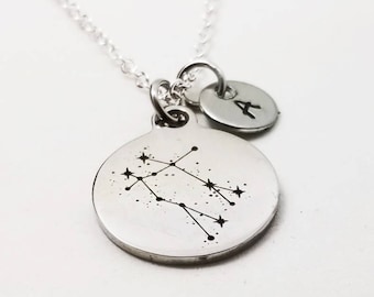 May include: Silver necklace with a Gemini constellation charm and a small initial charm. The initial charm is a silver disc with the letter 'A' engraved on it.