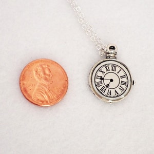 May include: Silver necklace with a round clock pendant. The clock face has Roman numerals and black hands. The pendant is about the size of a US penny.
