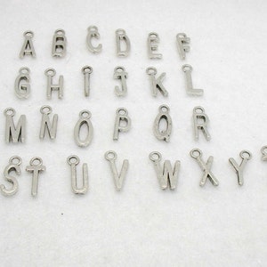 May include: A collection of silver-colored alphabet charms, each with a small loop at the top for attaching to jewelry or other crafts. The letters A through Z are displayed, offering a variety of options for personalization.